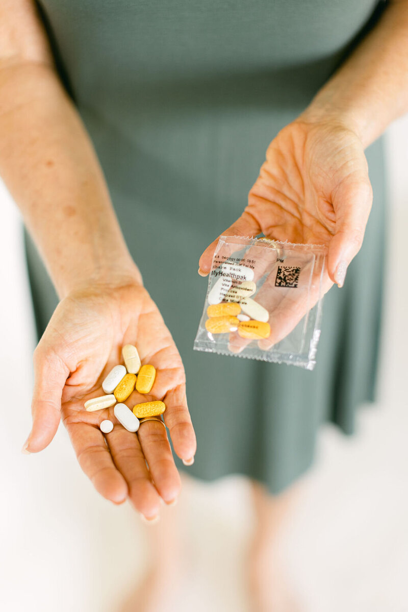 A person holding a variety of pills in one hand and a packet labeled 'MyHealthPak' in the other, possibly to illustrate a health or nutrition concept.