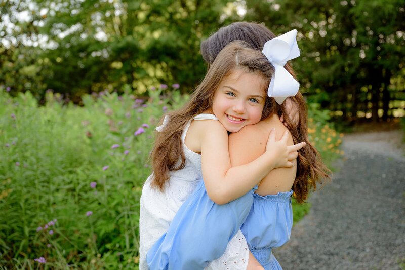 dark hair child hugs her mother with her cheek on her mother's shoulder