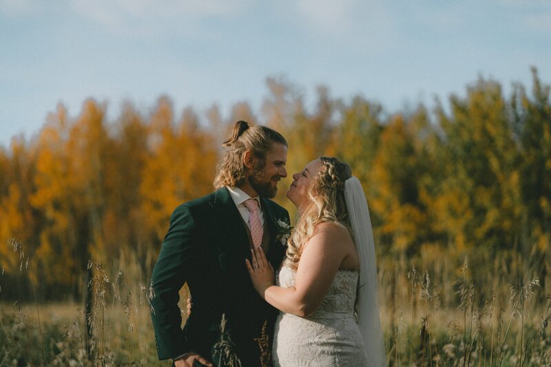 Wedding couple staring into each other's eyes in front of trees with autumn colours