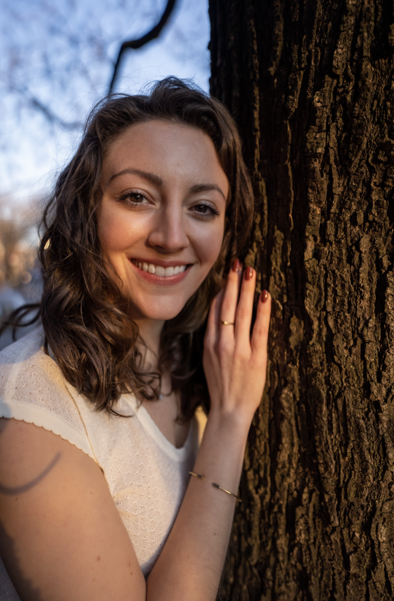 Woman with curly hair smiling with hand on tree