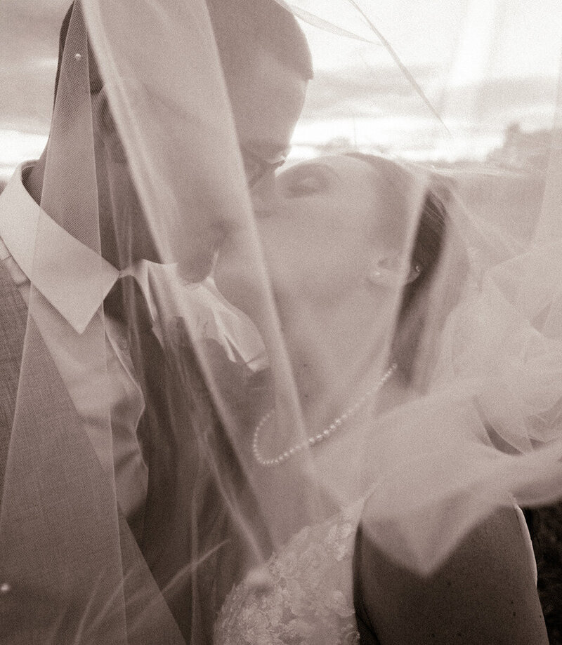 Veil shot - black and white photo of bride and groom kissing
