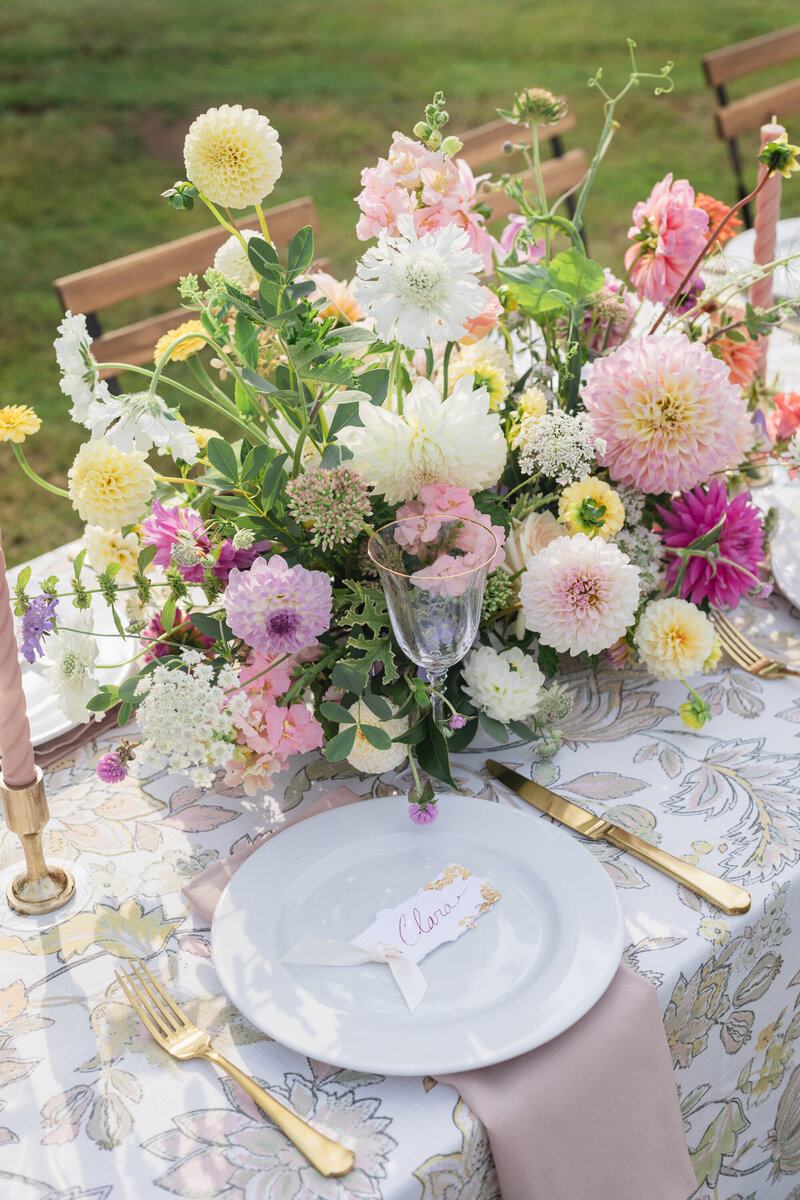 Outdoor table setting with colorful flowers, gold cutlery.