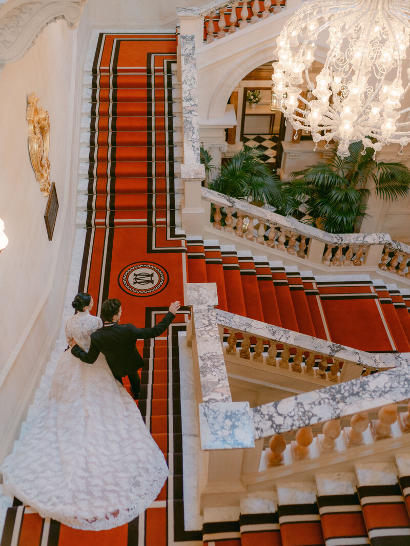 A couple walking together down the famous staircase on their wedding day at Raffles at The OWO London Hotel, captured from above.