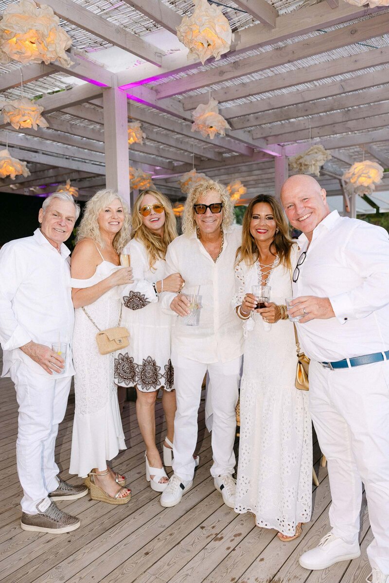 A group of guests laughing, all dressed in white. Among them a member of Bon Jovi band.