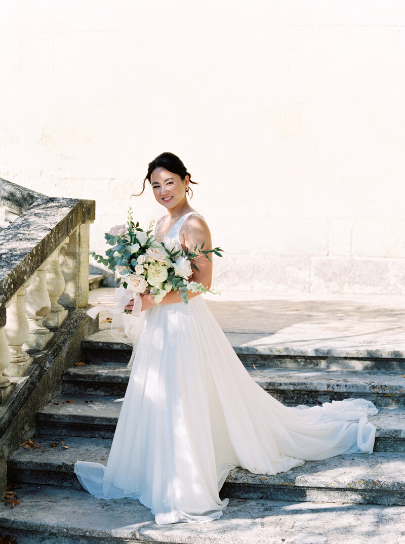 Bride stands on stone staircase in wedding gown holding her wedding bouquet