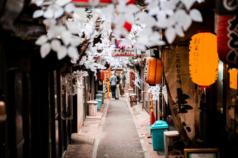 Narrow Tokyo alleyway decorated with hanging lanterns and paper blossoms, capturing local charm and evening ambiance