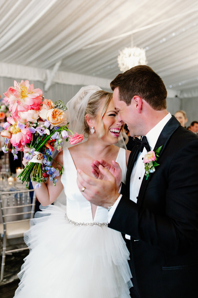 Bride and groom embrace while holding brightly colored wedding bouquet