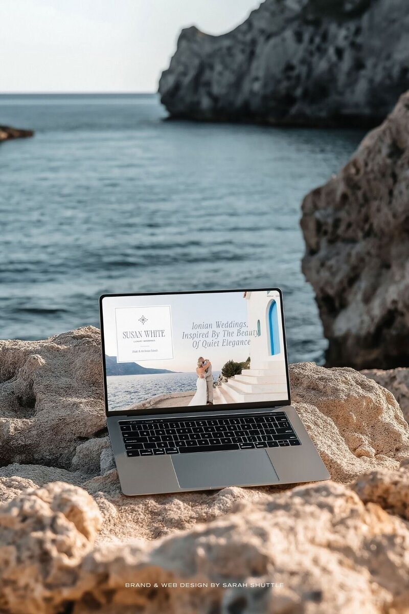 Laptop mockup of the Susan White Luxury Weddings website shown by the sea, echoing the Ionian-inspired colour palette and understated luxury style.