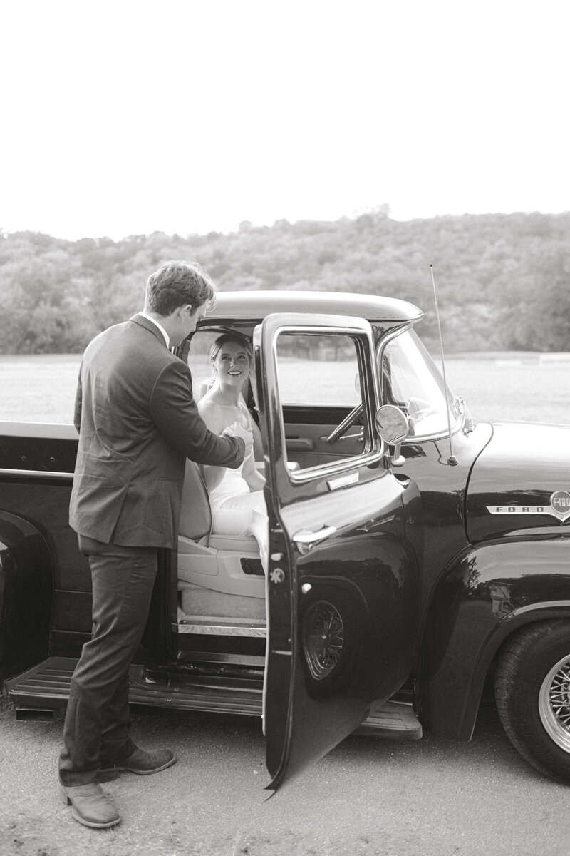 Black and white image of groom helping bride out of a vintage truck
