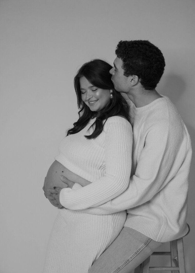 Family of four hug and the toddler boys rub their mother's pregnant belly.