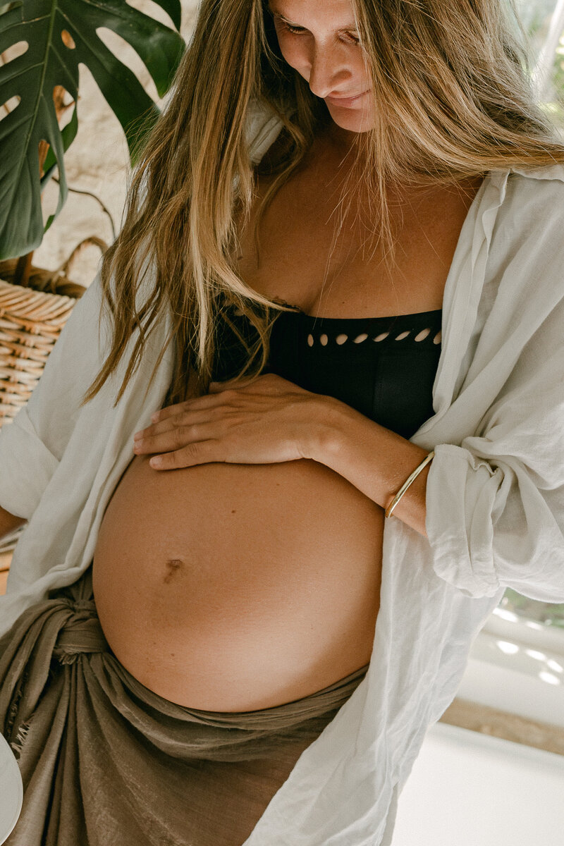 In home maternity photoshoot. Mother looking down and holding her pregnant belly. 