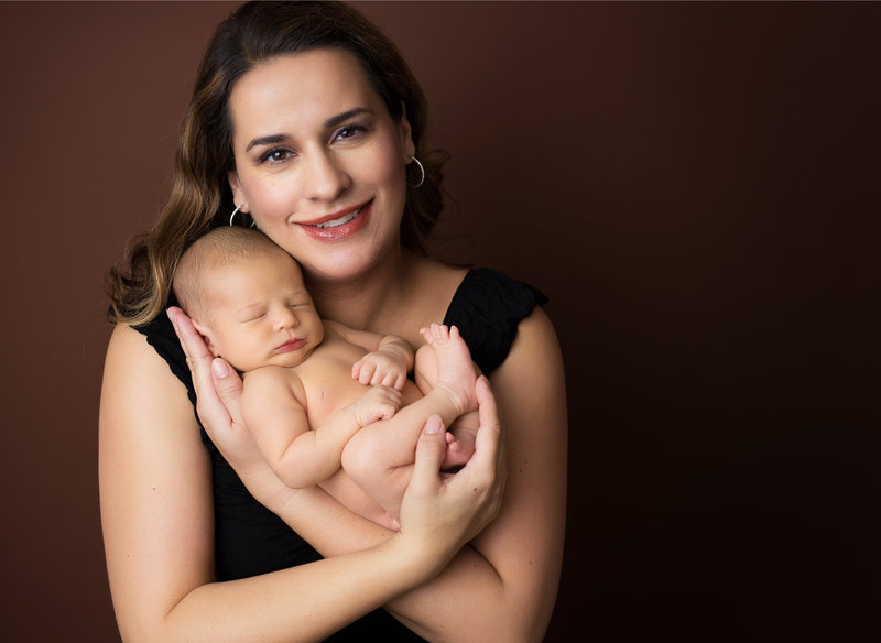 mom holding newborn boy with brown background
