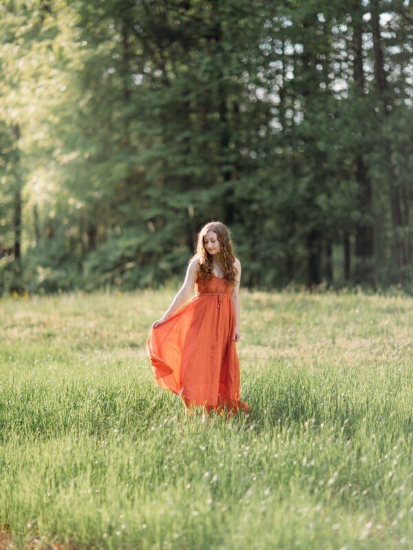 Senior Portrait of a girl in grassy field twirling her orange dress