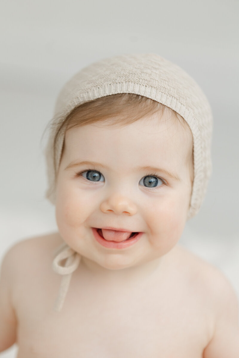 12 month old little girl smiles wearing a bonnet