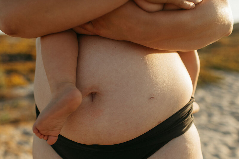 Close-up of Molly's baby resting on her arm, with a focus on Molly’s bare belly and the baby’s feet