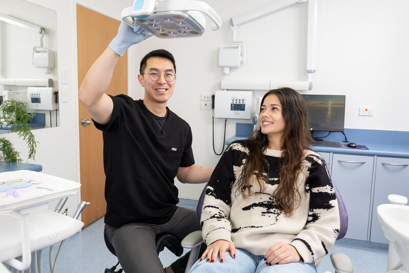 Dentist holding light while smiling, with happy patient beside him