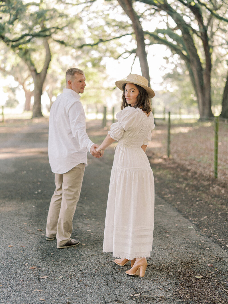 A couple on a road holding hands with the women looking back at the camera.