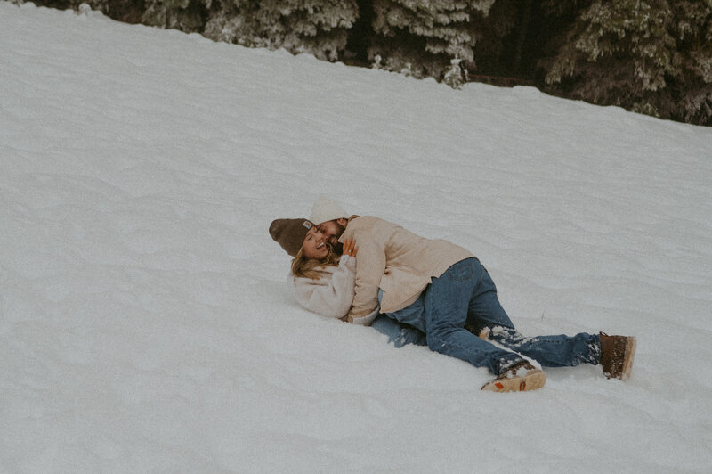 couple rolling around in the snow during their engagement photos near Black Butte Ranch