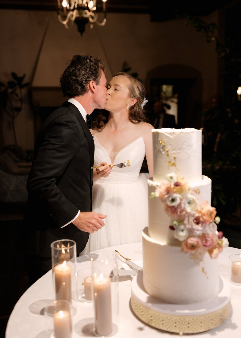 November wedding at Graylyn Estate, designed and planned by Charming Carolina — bride and groom sharing a kiss after cutting their three-tiered wedding cake in the sun room.