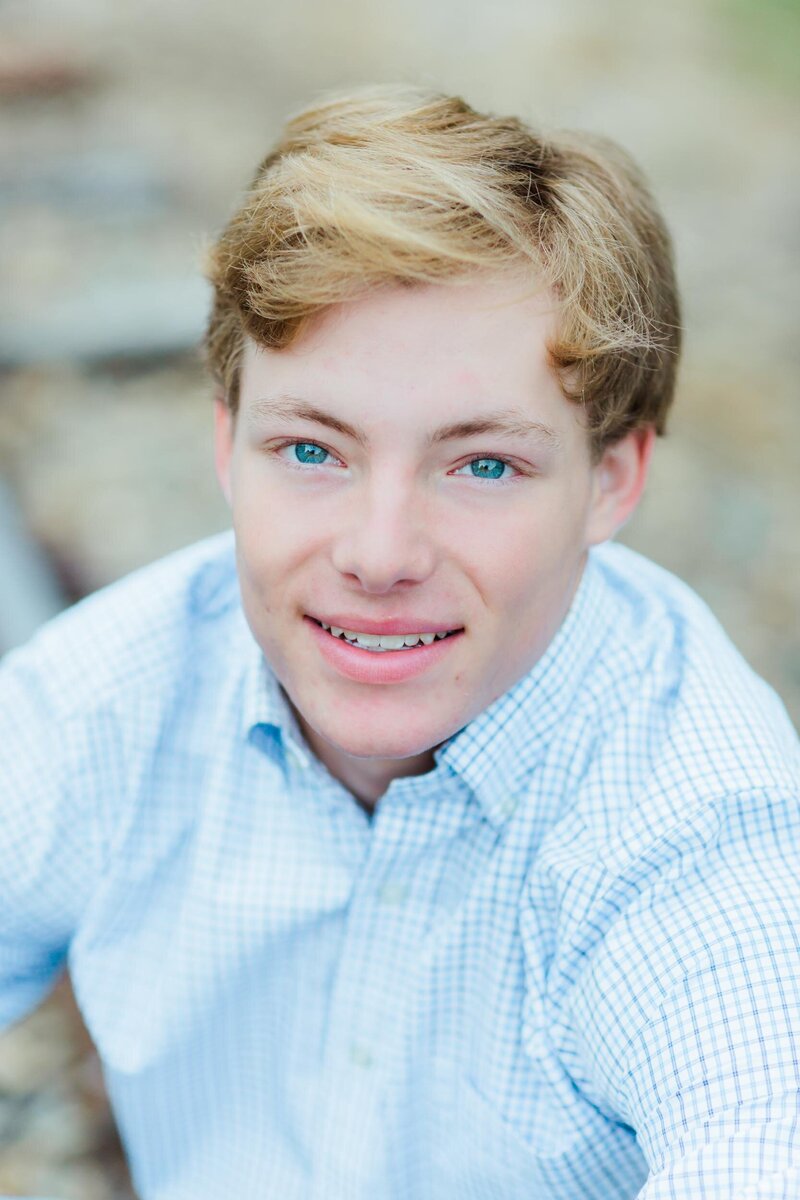 A handsome young man smiles up a the camera with blue eyes during his senior portrait session with Salina Korn Photography.
