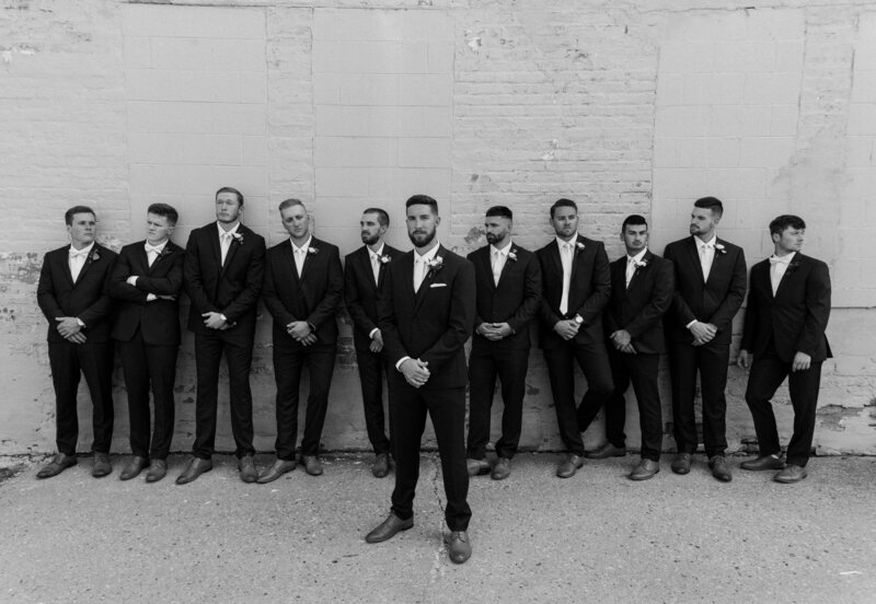 black and white photo of groomsmen lined up on wall  in suits