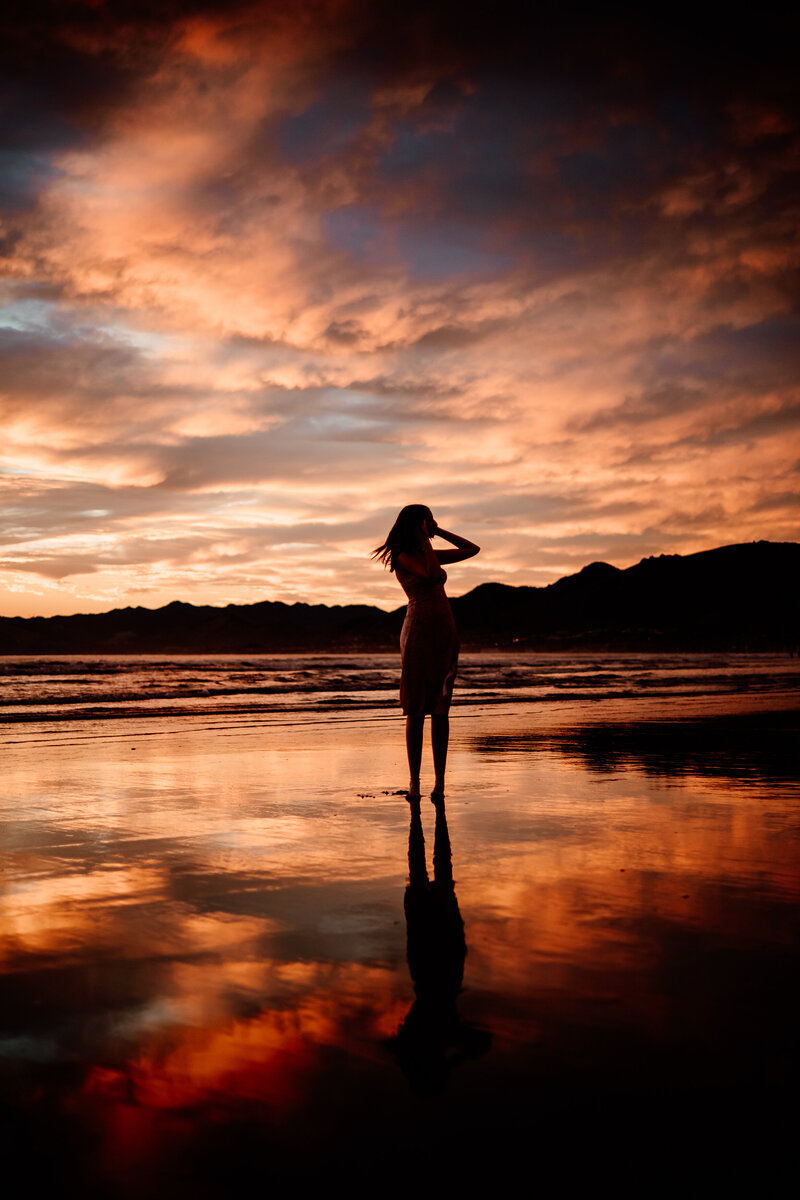 Senior girl silhouetted against a colorful beach sky