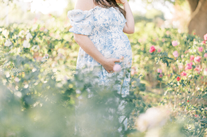 pregnant mom in blue dress holding belly surrounded by roses.