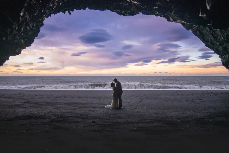 A couple in wedding attire is seen through a cave on Black Sand Beach Reynisfjara in Iceland.