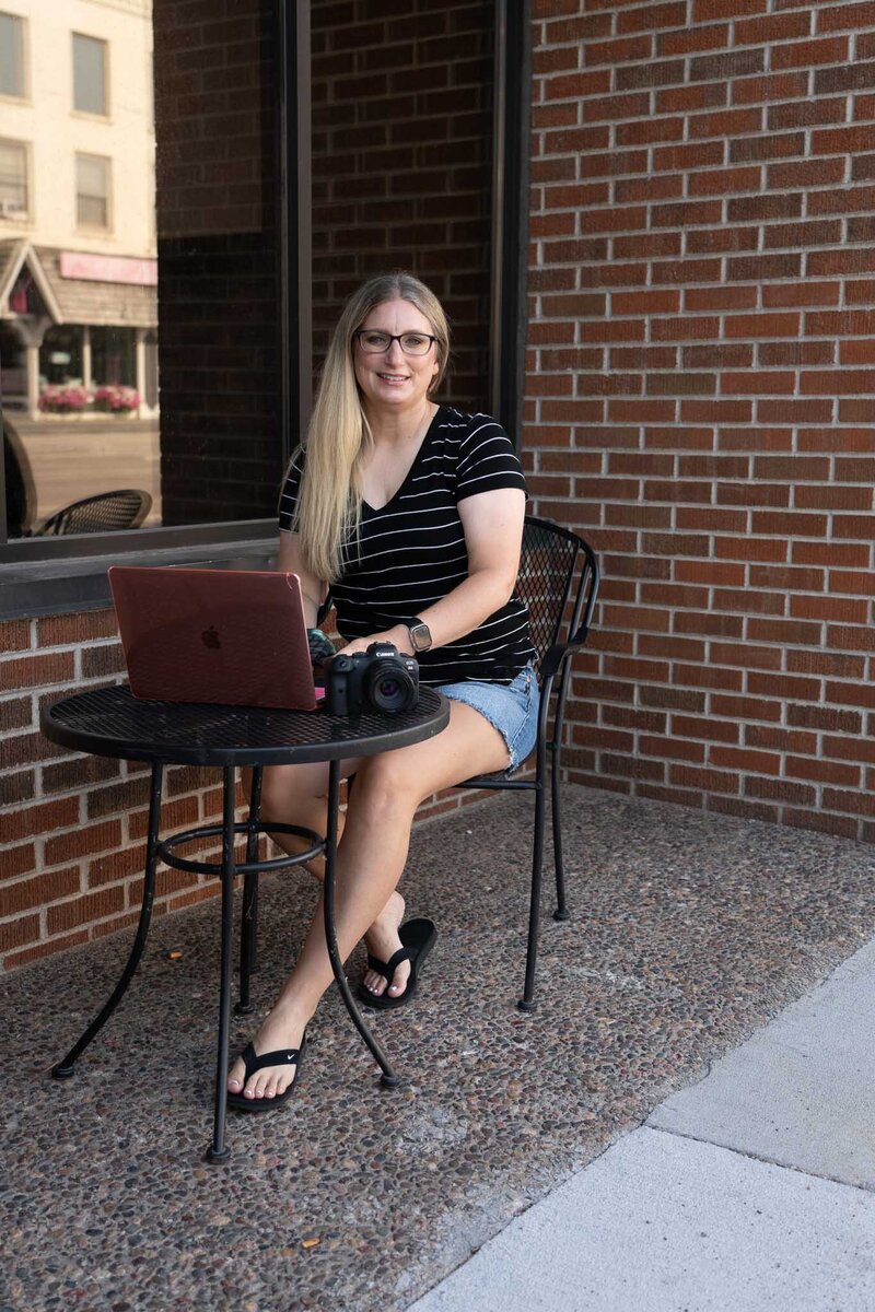 Megan smiling while sitting at an outdoor café table with her laptop | Senior Photographer in Lawrence, KS