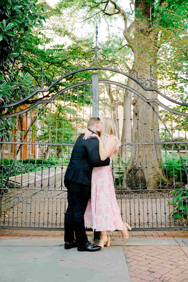 A couple in wedding attire stands hand in hand in a lush garden, with a majestic Gothic-style cathedral in the background. The scene is peaceful and romantic.