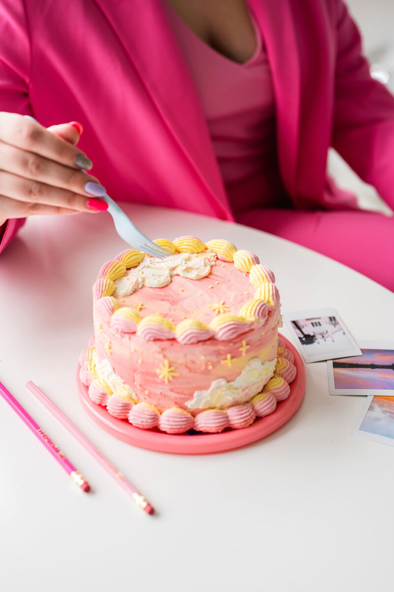 Hand holding a plastic fork up to a pink and yellow cake