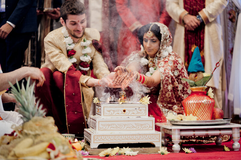 groom and bride pouring rice over a sacred fire during their Indian wedding ceremony - Laaja Homam - both dressed in colourful traditional Indian dress