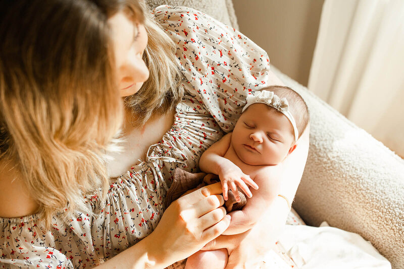 baby swaddled in a tan swaddle mom in a floral dress snuggled into her newborn baby with her eyes closed