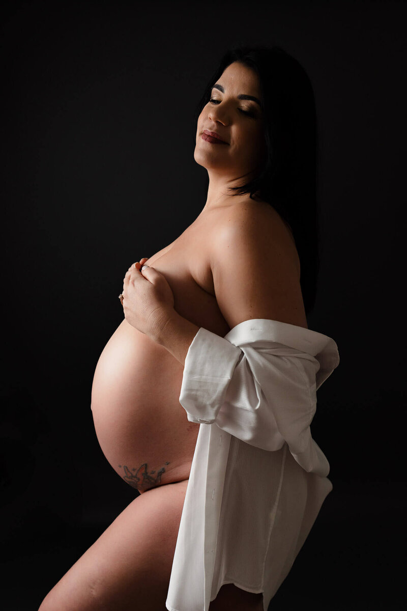 A mom-to-be posing in a Gainseville photography studio in nothing but a white button up shirt.