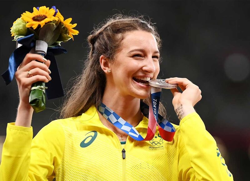 Australian athlete smiles while biting silver medal and holding sunflower bouquet on Tokyo 2020 Olympic podium