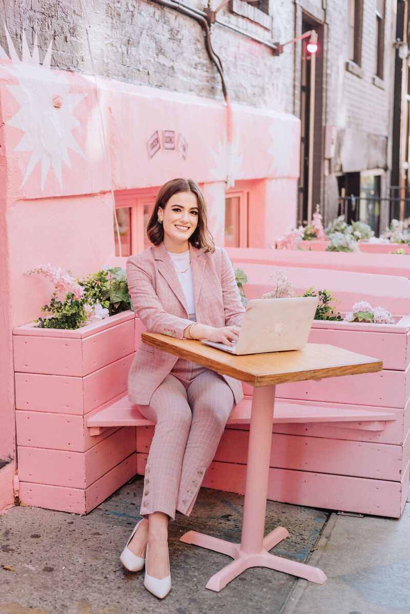 Madison sitting at a table outside working on a laptop smiling