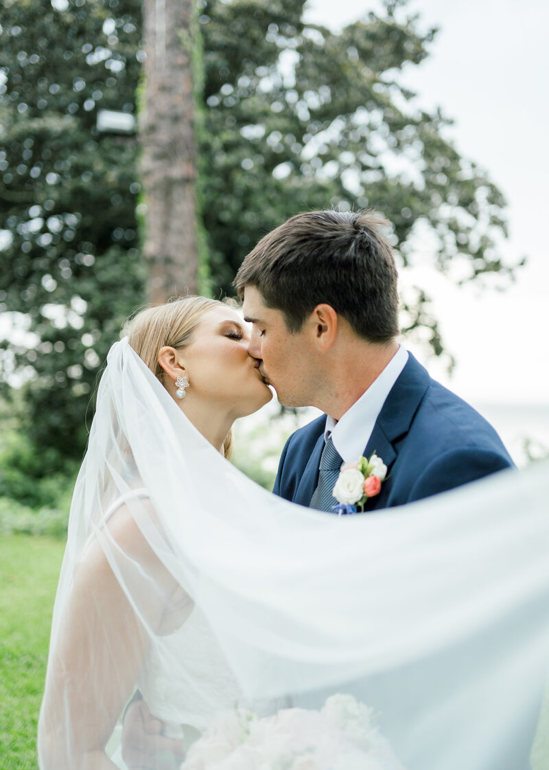 bride and groom kissing while wrapped in veil