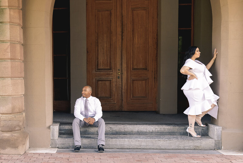 The engagement couple is posing separately in a doorway. The couple is wearing white and gray. The couple are lovely.
