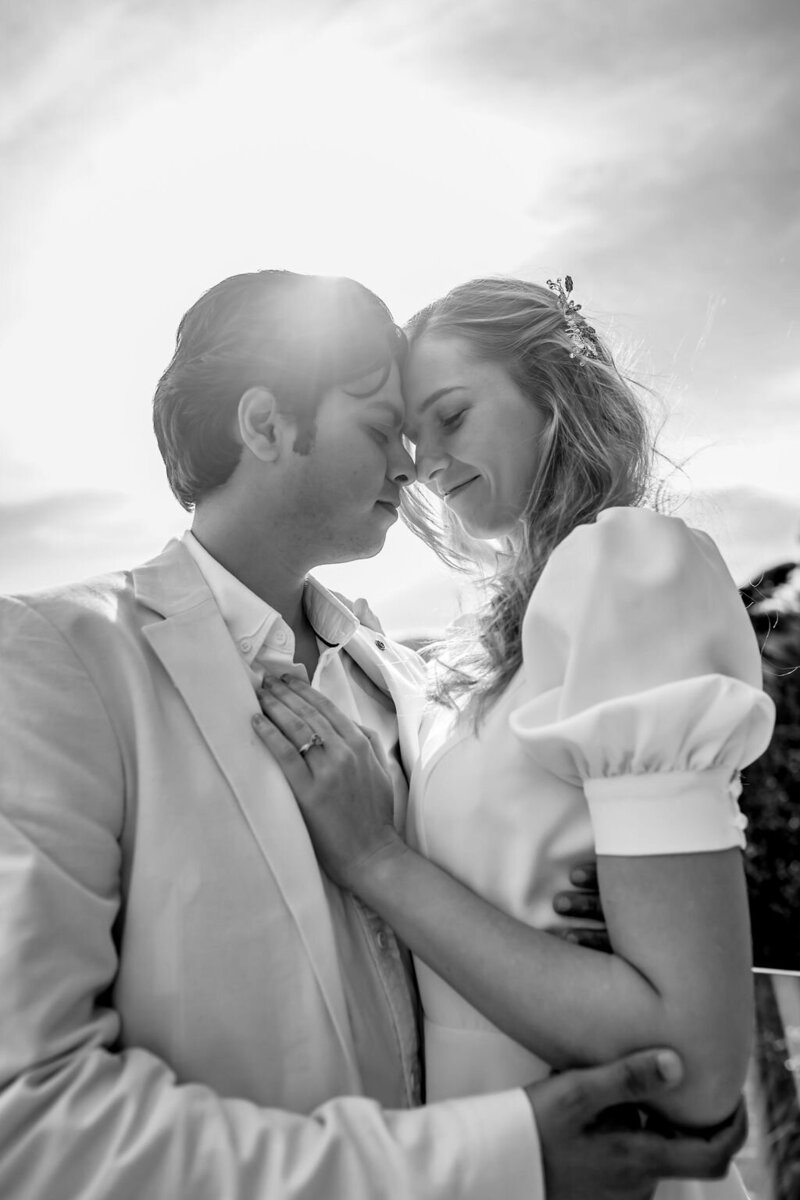 Black and white close up image of couple with their heads together and the sun shinning just behind them captured by Zanthe Vorsatz Photography