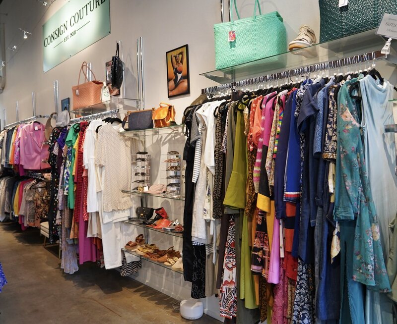 The wall of a store with clothing racks, shoes, accessories, and purses 