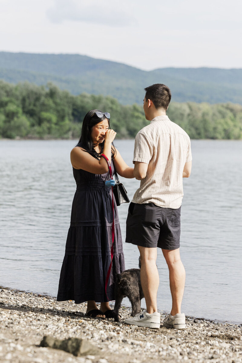 Emotional reaction just after a riverside proposal in the Hudson Valley with the couple's dog at their feet