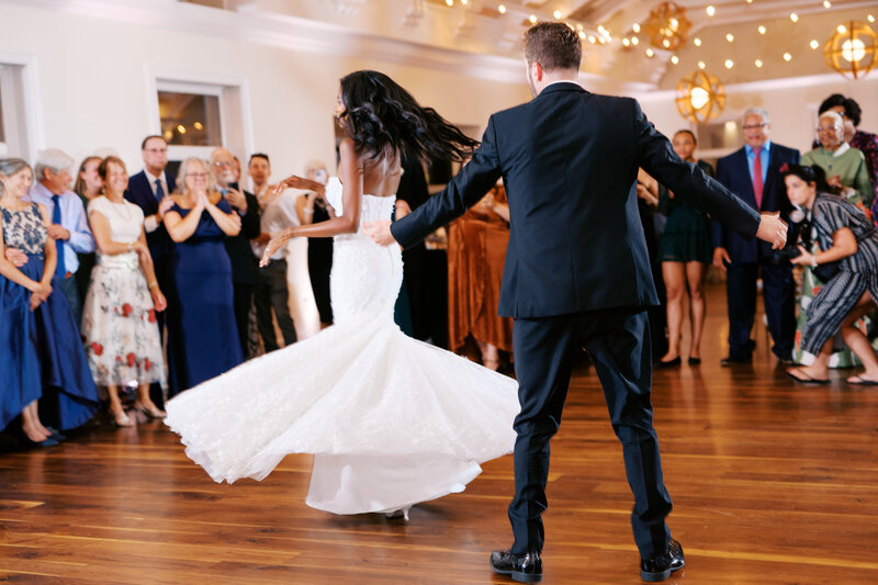 Groom twirls bride beneath wicker lanterns on checkboard dance floor at Glen Foerd Estate in Philadelphia, PA