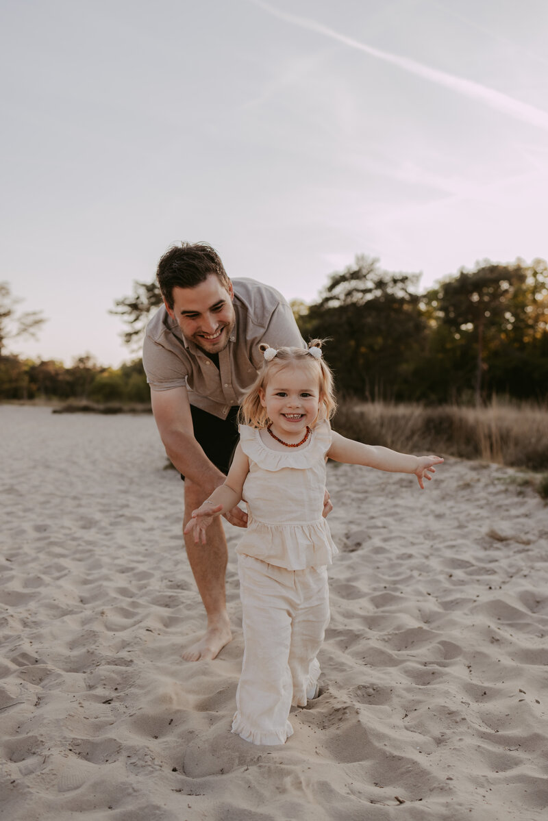 papa speelt met kind in het zand op bedaf