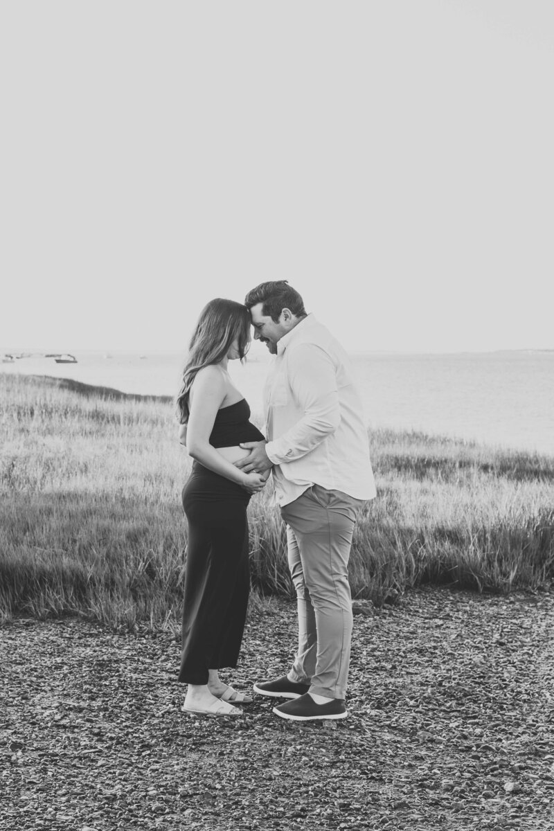 Husband and wife posed sideways with husband's hands on wife's belly during maternity photoshoot.