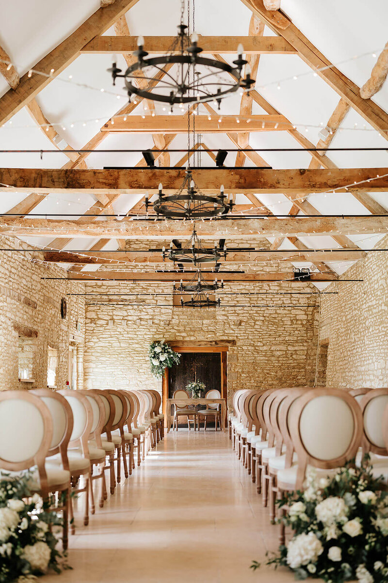 Aisle inside Caswell House barn ceremony with fairy lights and floral arrangements