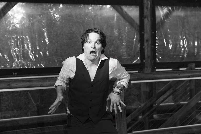 A groom wearing a shirt and vest makes a funny face while dancing on the dance floor