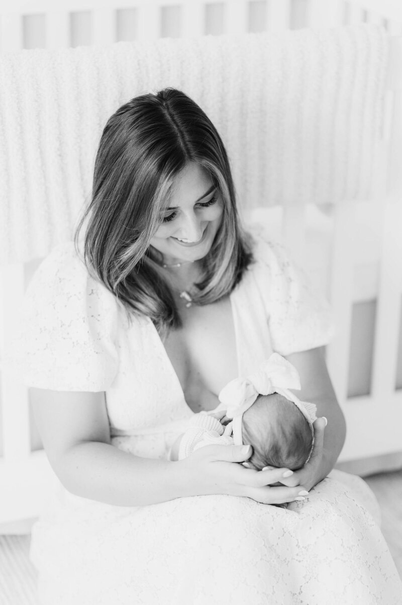 Newborn girl being held by mom in front of crib taken in Douglas, MA by the best newborn photographer in central Massachsuetts