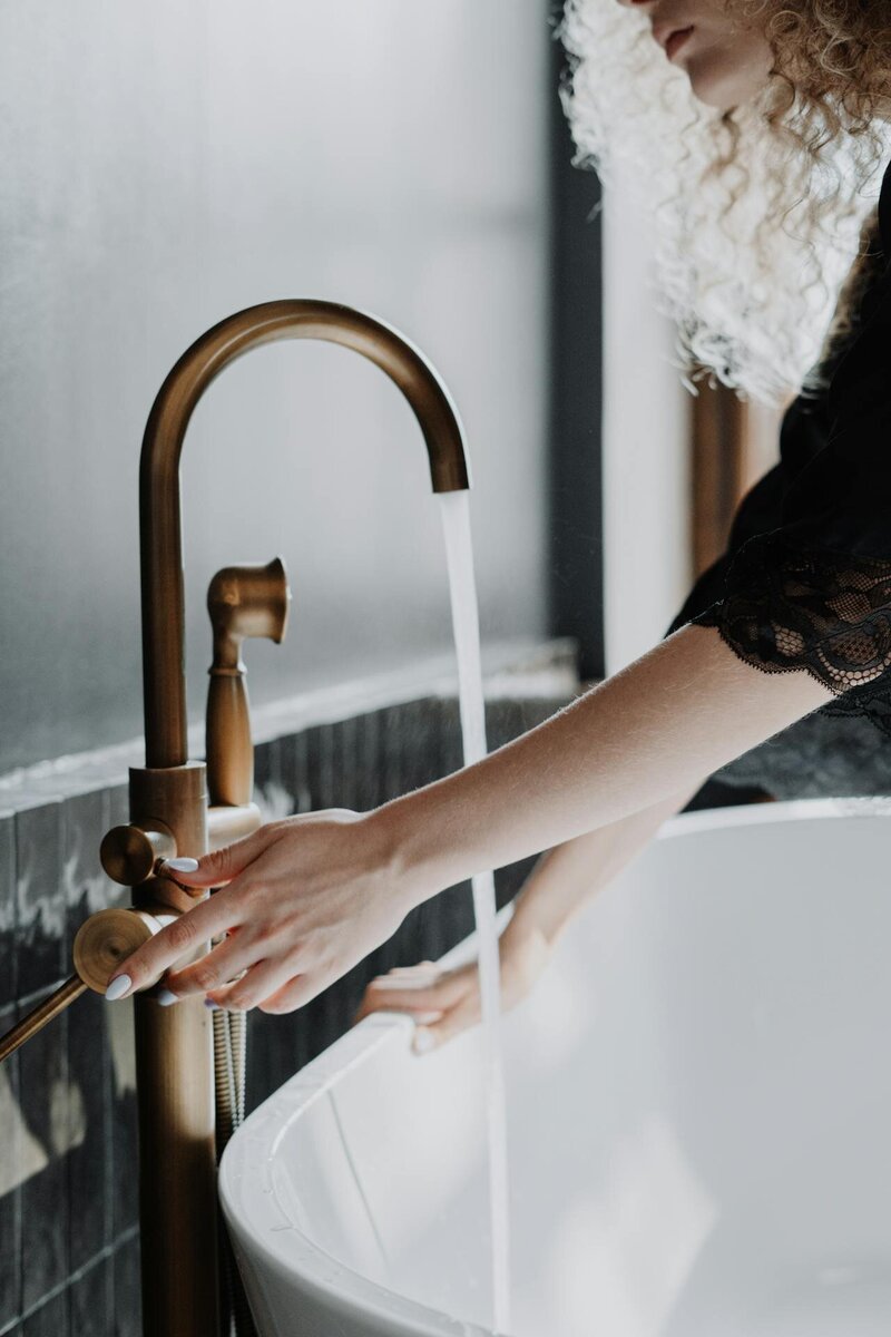 a bronze kitchen sink faucet with a woman turning on the hot water and the water running in the sink.