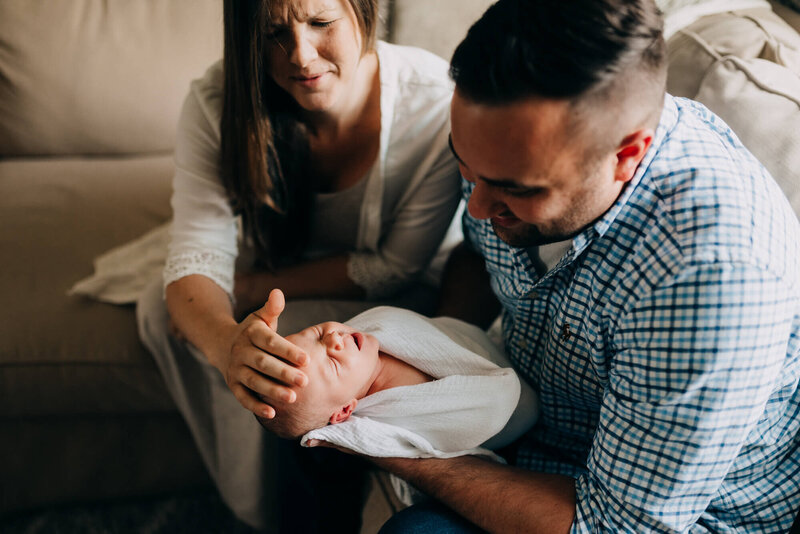 mom and dad holding newborn baby on the couch and baby is yawning