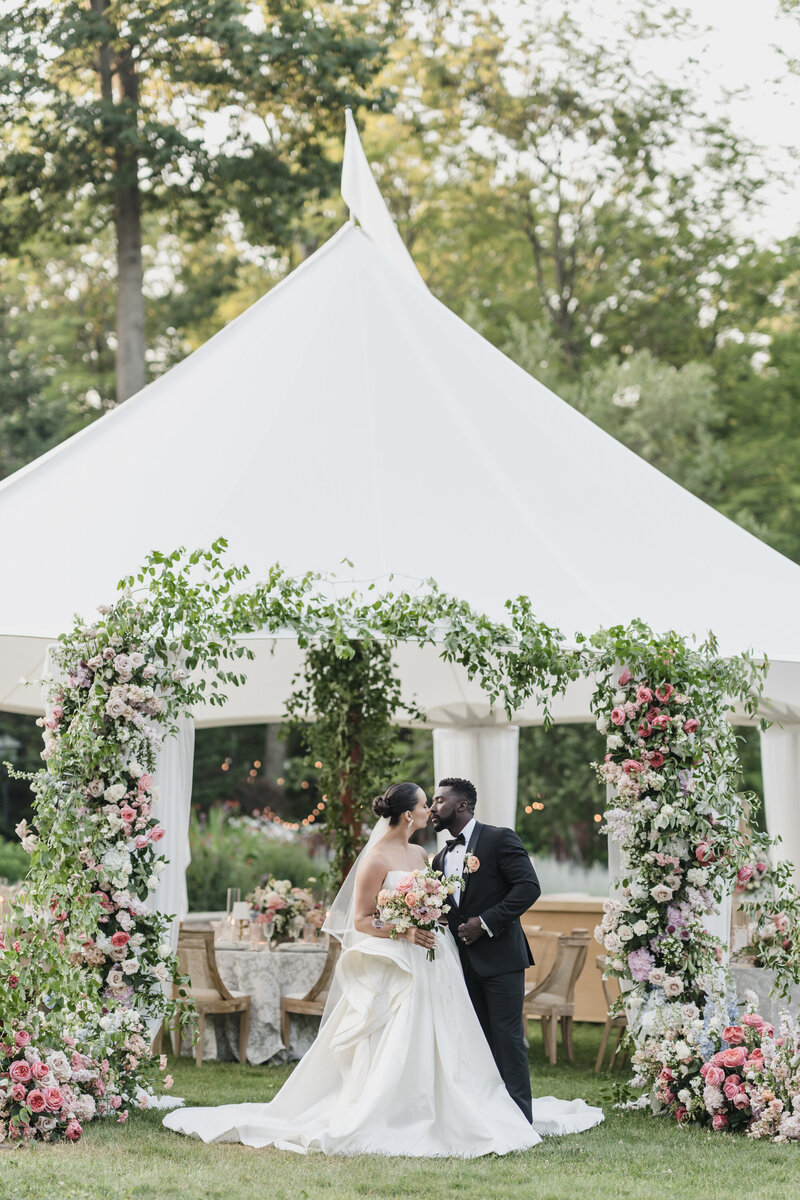 Bride and groom pose beneath an arched window with checkered flooring, bathed in natural light and classic architectural charm.